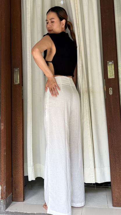 Woman in black top and white Lily pants standing in a doorway with curtains.